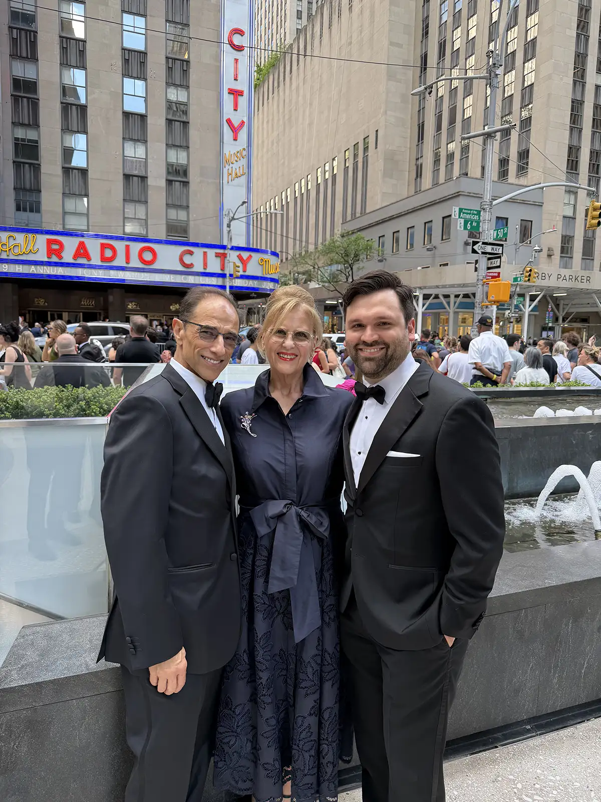 Color photo of Hal Luftig, Cathy Dantchik, and Kevin Connor in formal evening wear standing in front of Radio City Music Hall in New York City